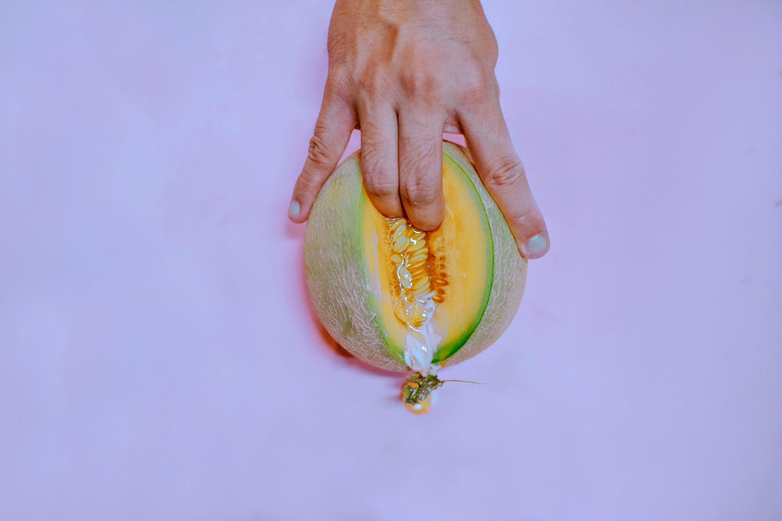 Fingers penetrating the inside of a cantaloupe melon